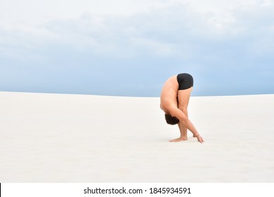 Young man performing a yoga pose Uttanasana on the beach