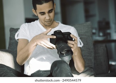 Young man photographer sits on a couch at home, reviewing photos on his digital camera with focus and passion, bathed in natural light - Powered by Shutterstock