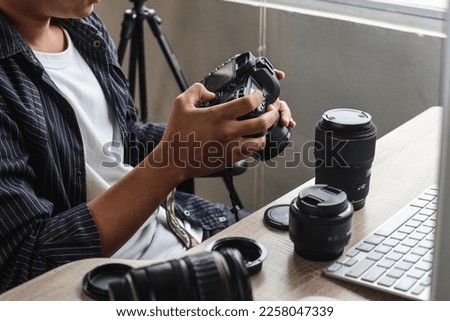 Young man photographer sitting and press button of professional camera to review shoot or setting camera at home office studio. 
