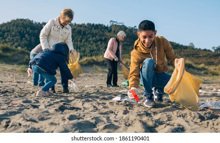 Young man picking up trash with group of volunteers on the beach - Powered by Shutterstock