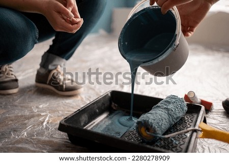 Young man picks up a can of dark blue paint and pours it into a tray, close-up. Room renovations at home. Cl