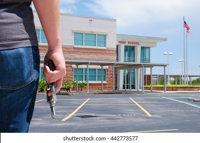 A young man with a pistol gun is standing in front of a high school preparing to commit a crime