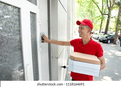 Young Man With Pizza Boxes Ringing The Doorbell Outdoors. Food Delivery Service