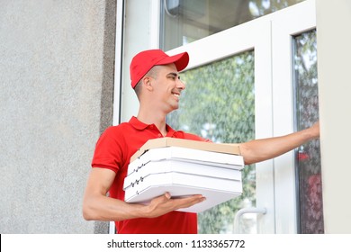 Young Man With Pizza Boxes Ringing The Doorbell Outdoors. Food Delivery Service