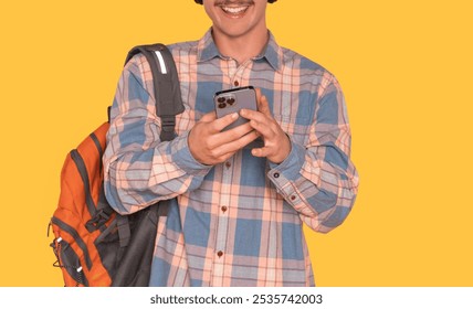 A young man in a plaid shirt and backpack enjoys his mobile phone against a bright yellow background - Powered by Shutterstock