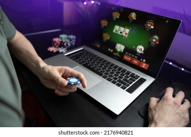 Young man play online poker in laptop. Unrecognizable person in neon light.