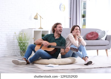 Young man playing acoustic guitar badly for displeased girlfriend in living room. Talentless musician - Powered by Shutterstock