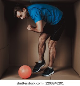 Young Man Playing With Ball In Cardboard Box. Sports And Healthy Lifestyle. Life In Little Cardboard Box. Uncomfortable Life. Personal Spase Concepts. Young Introvert. Man In Sportswear.