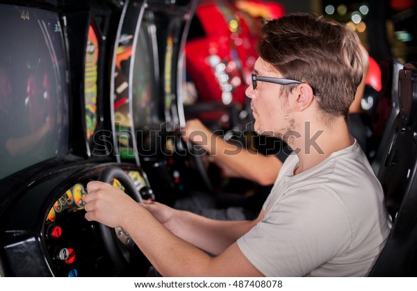 Young\
man playing driving wheel video game in game\
room
