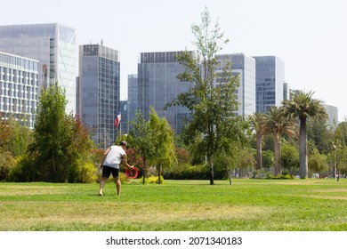 Young Man Playing With Flying Ring On Sunny Day At The Park And Financial Buildings On Background. Joy Versus Work Stress Concepts