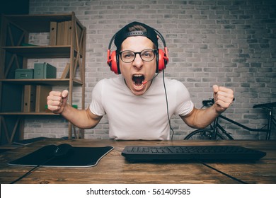 Young man playing game at home and streaming playthrough or walkthrough video. Stylish boy screaming because of fail. He is going to make revenge that's why he is holding his fists in attack position