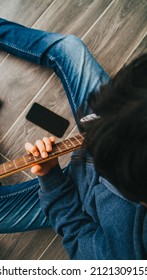 Young Man Playing Guitar And Learning From His Phone