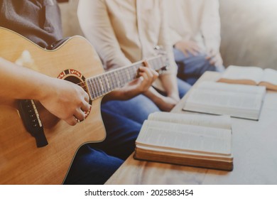 A young man is playing guitar and sings a song from a Christian hymn book with his friends at home, Christian family worship concept