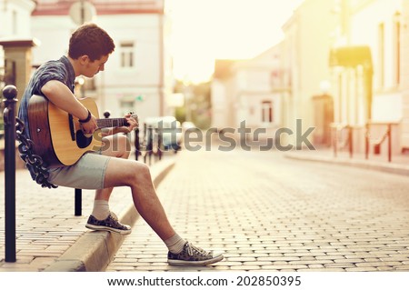 Young man playing on acoustic guitar - outdoor