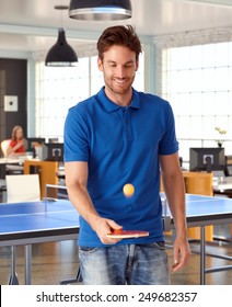 Young Man Playing Ping Pong In Office, Smiling.