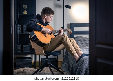 A Young Man Plays The Acoustic Guitar In His Room At Home.