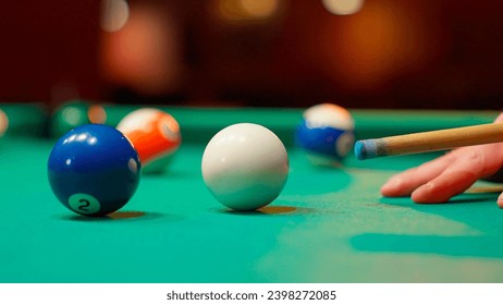 A young man plays American billiards. Russian billiards, an American in a billiards club and bar. Dark colors in the billiard club. A man pockets snooker balls.