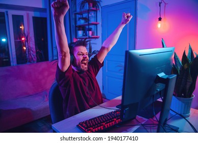 Young Man Plays Computer Games At Home.  Neon Streamer Studio. The Guy With The Headphones Is Having Fun On The Internet.