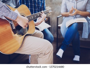 Young Man Plays Guitar And His Friends Sing A Song While Praise And Worship God Together Indoor, Christian Family Or Small Group Fellowship In Home And Working Place Concept