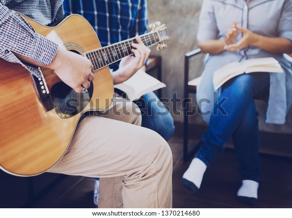 Young man\
plays guitar and his friends sing a song while praise and worship\
God together indoor, christian family or small group fellowship in\
home and working place\
concept