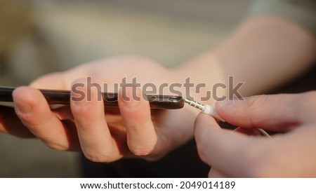 Young man plugging aux input cable into his smartphone, listening to music or making a call close-up