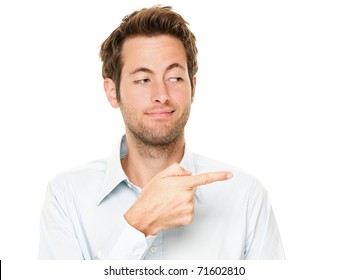 Young Man Pointing A Bit Sneaky Looking At Copy Space. Handsome Young Caucasian Businessman Isolated On White Background.