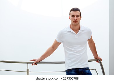 Young man in a polo shirt stands leaning on railing