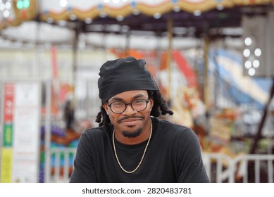 A young man posing for the camera while standing in front of a carousel in a county fair.