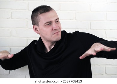 Young man posing confidently in a black sweater against a textured white brick wall expressing creativity and passion for art. - Powered by Shutterstock