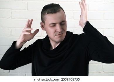 Young man posing confidently in a black sweater against a textured white brick wall expressing creativity and passion for art. - Powered by Shutterstock