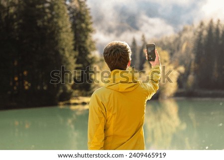 Young man posing for a selfie at mountain lake in Jezersko. Adventure travel in Slovenia. Smartphone photography in beautiful autumn setting. Influencer creating social media content.