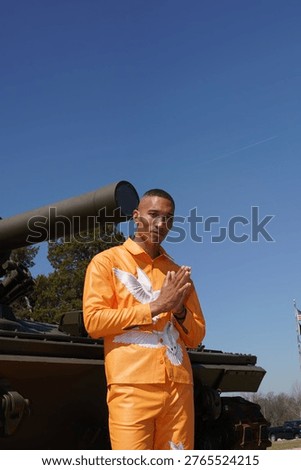 A young man posing while standing in front of a decommissioned army tank.          