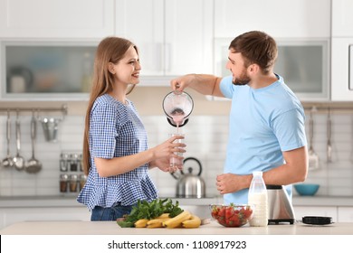 Young Man Pouring Delicious Milk Shake Into Glass For His Girlfriend In Kitchen