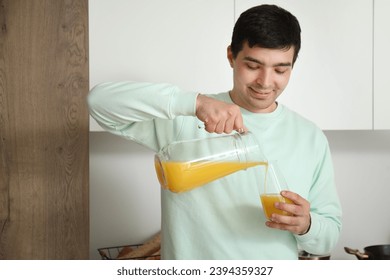 Young man pouring orange juice into glass in kitchen - Powered by Shutterstock