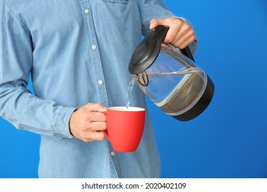 Young Man Pouring Water From Electric Kettle In Cup On Color Background