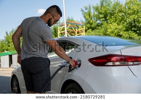A young man pours gasoline into the gas tank of a white car.A young man pumps gasoline into a gas tank. Fuel and oil crisis. The concept of gasoline prices and the oil crisis.