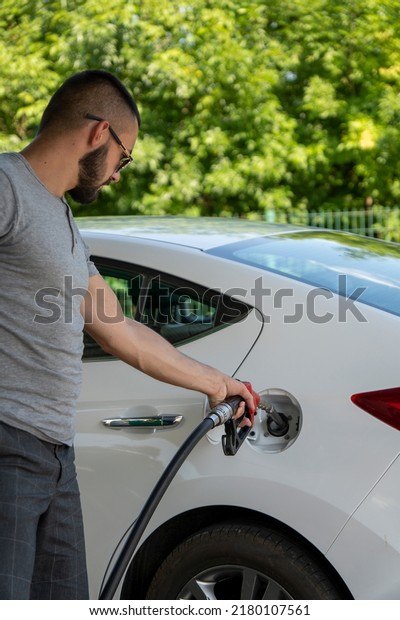 A young\
man pours gasoline into the gas tank of a white car.A young man\
pumps gasoline into a gas tank. Fuel and oil crisis. The concept of\
gasoline prices and the oil\
crisis.
