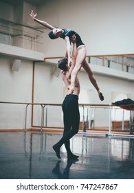 Young Man Practicing In Classical Ballet With Young Beautiful Woman In Black Clothing In The Gym Or Ballet Hall. Couple Jumping Dancing Sensual Dance. Minimalism Interior,