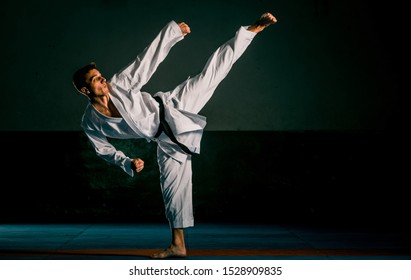 Young man practicing his karate moves, doing a high kick while standing still wearing white kimono and black belt - Powered by Shutterstock