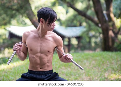 Young Man Practicing Kung Fu With Nunchaku In A Park In Hong Kong.