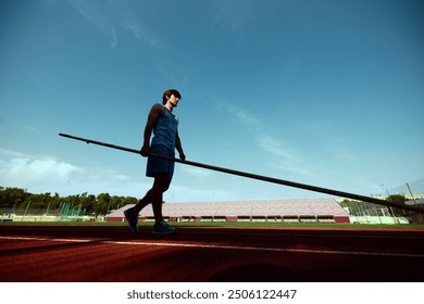 Young man practicing pole vaulting with determination at outdoor stadium track, athlete preparing for intense training session. Concept of sport, competition, tournament, active lifestyle, strength - Powered by Shutterstock