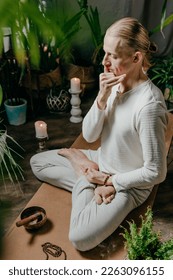 Young man practicing Surya Bhedana Pranayama sitting in Lotus pose, asana mat with closed eyes indoor. Yoga warming breathing.