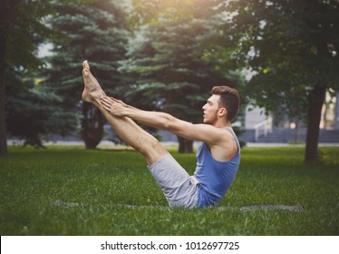 Young Man Practicing Yoga In Boat Pose On Green Grass Outdoors, Making Corner Stretching Exercise, Copy Space