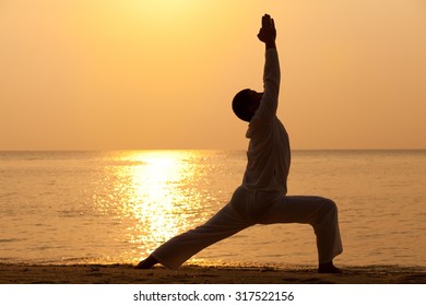 Young man practising yoga at the beach - warrior I pose.
