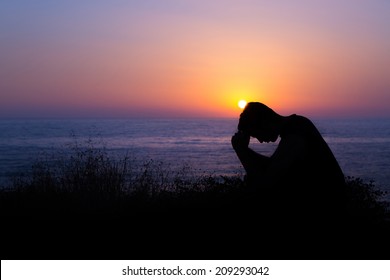 Young man praying to God during sunset by the sea