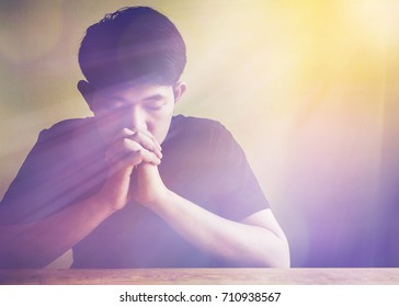 Young man praying on wooden table with window light bokeh, christian background with copy space