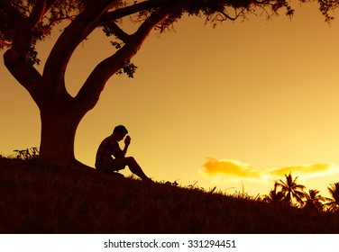 Young man praying under a tree. 