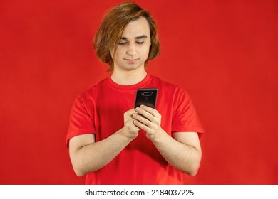 Young Man Prep Student With Long Hair. 20s Guy With Smartphone On A Red Background.