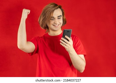 Young Man Prep Student With Long Hair. 20s Guy With Smartphone On A Red Background.