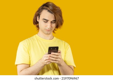 Young Man Prep Student With Long Hair. 20s Guy With Smartphone On A Yellow Background.